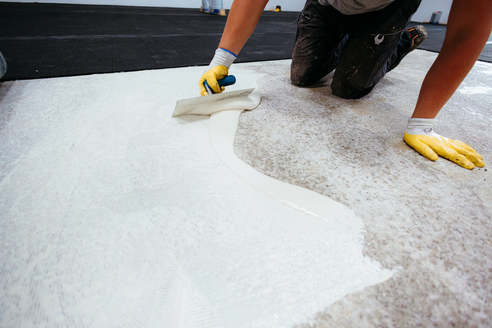 Professional flooring installer using a notched trowel to apply commercial-grade adhesive to a concrete slab.