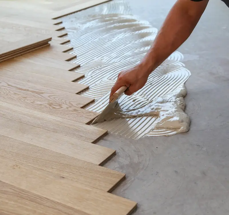 Professional installer applying adhesive and laying LVP flooring with precision.